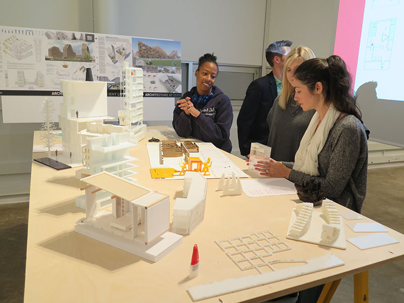 Architecture students lean on a table holding 3D-printed building models.