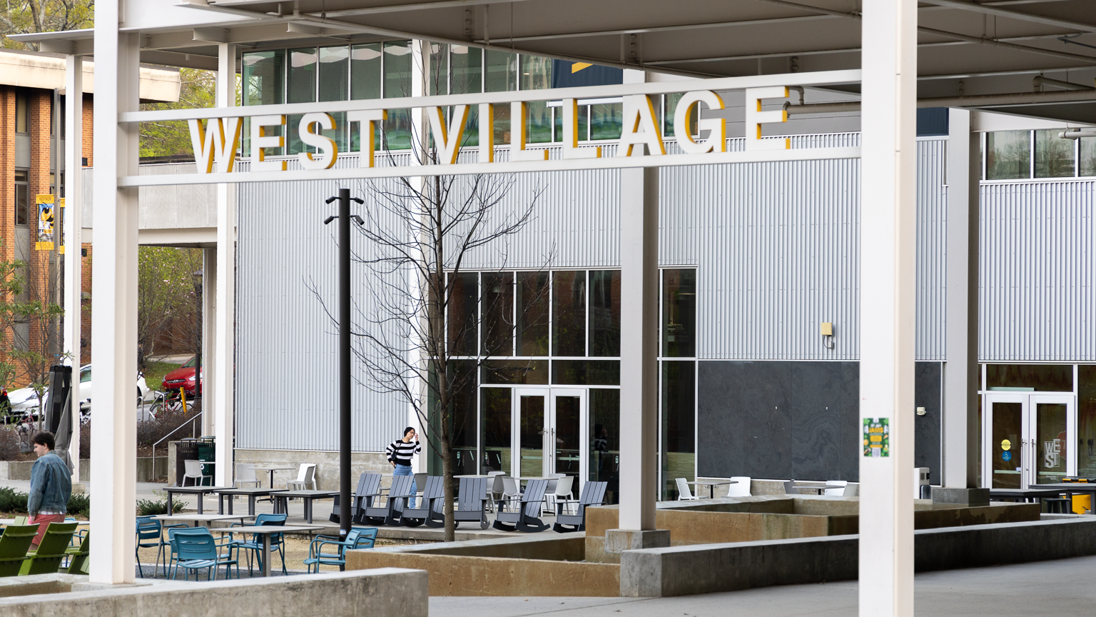 Entryway of West Village complex, showing the West Village sign and the music wing in the background